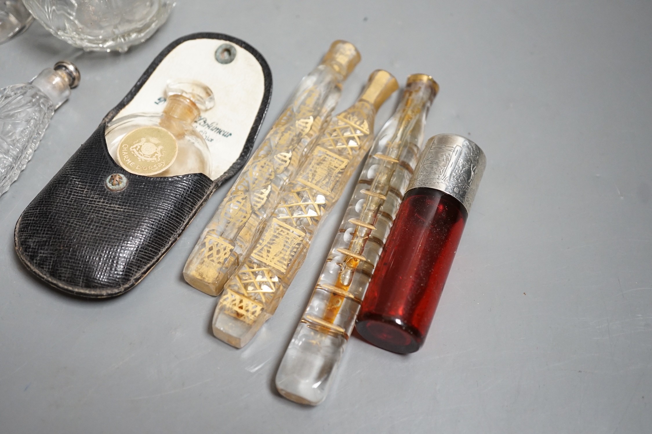 A late Victorian silver mounted ruby glass cylindrical scent bottle, engraved in the style of Kate Greenaway, Sampson Mordan & Co, London, 1887, 75mm, together with eight other assorted glass scent bottles, three with si